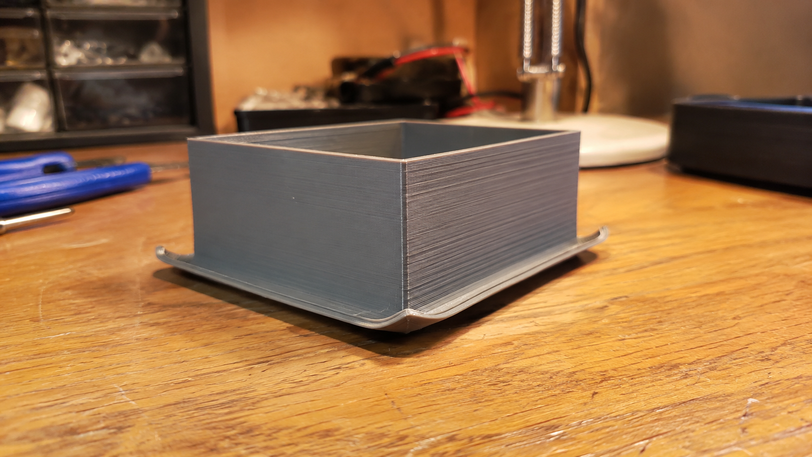 3D print corner lifting off the build plate with visible warping and brim attached -- 3D printing troubleshooting warping